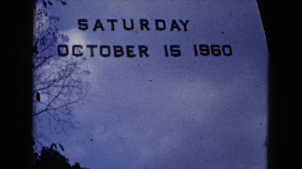 Wauconda 1960 home-movie title frame with block date lettering, blue sky, bare branches, dust specks, and soft 8mm texture.
