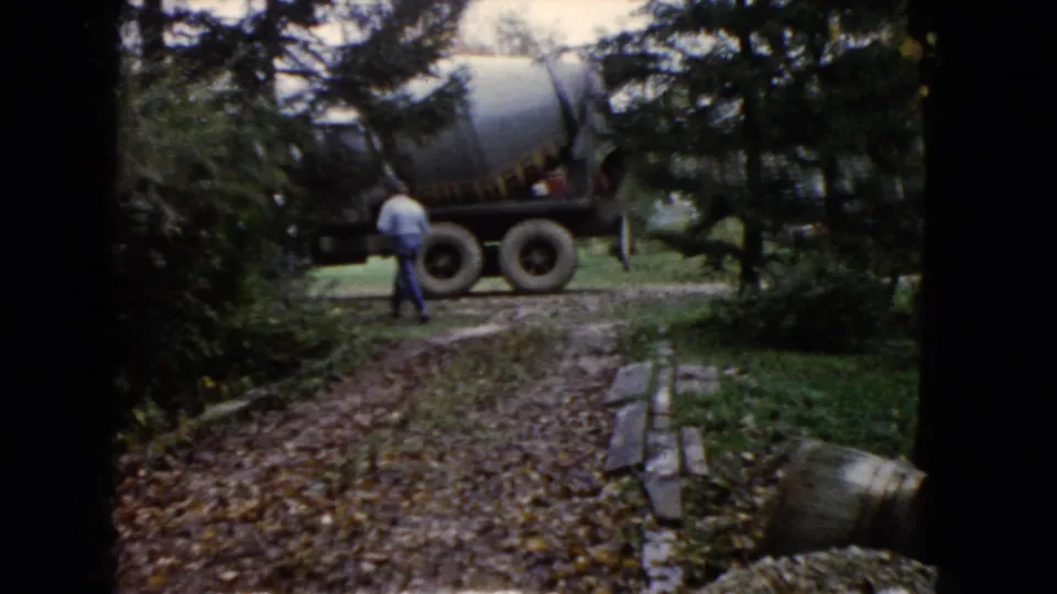 In Wauconda, Illinois home-movie footage, a concrete mixer truck sits by a leafy driveway as a person stands near it.