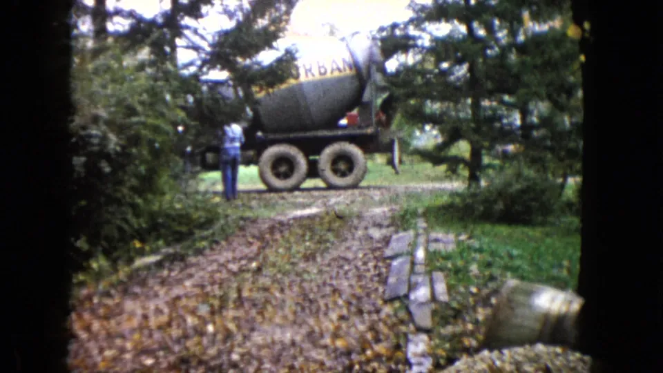 The concrete mixer truck remains parked near the leafy driveway, with one person visible among trees and shrubs.