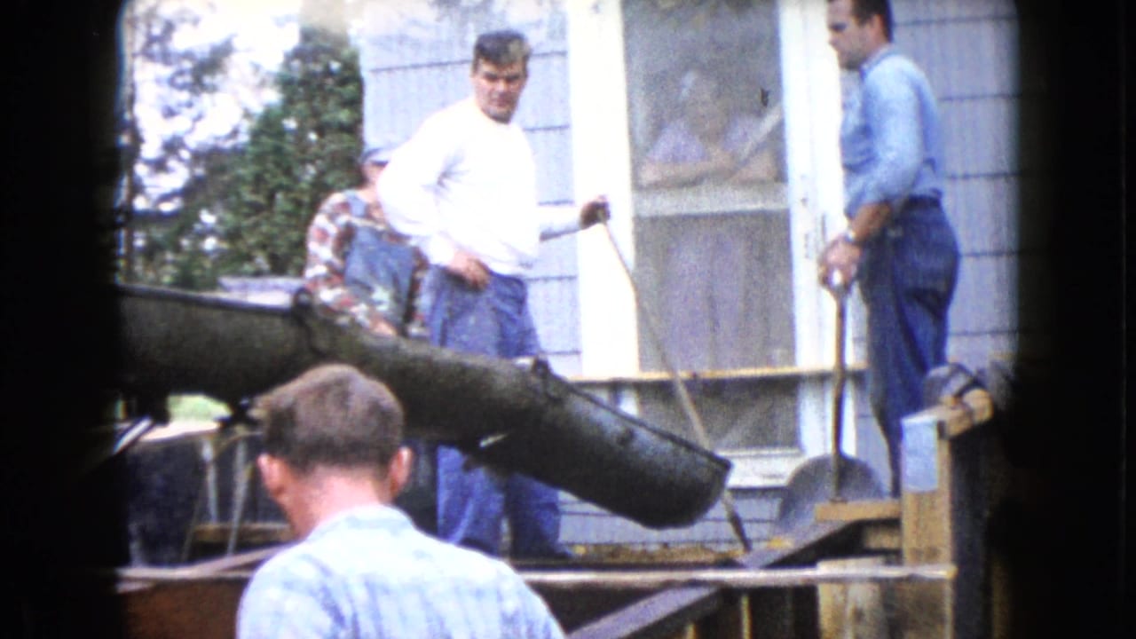 Men stand near a concrete chute and porch during a residential construction pour.