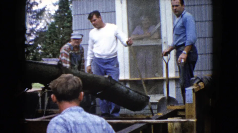 A 1960 Wauconda home-movie frame shows several men around a concrete chute at a residential construction site.