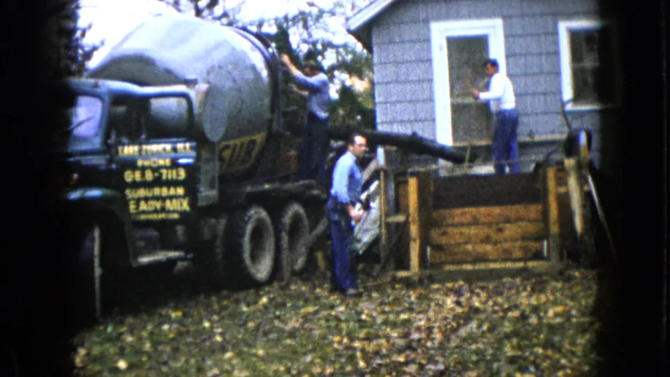 A worker checks the chute near the wooden form as another man stands by the doorway of the Wauconda house.