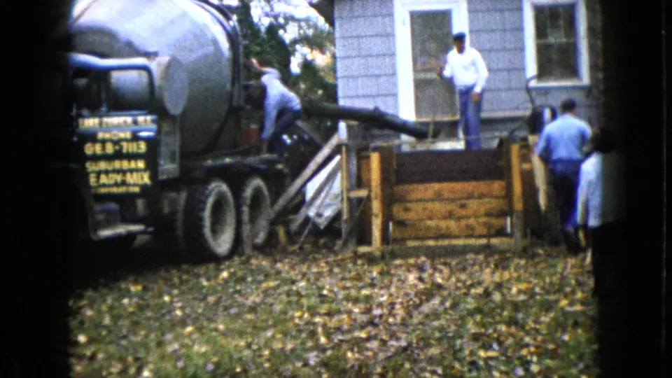 The mixer truck remains parked beside the Wauconda house as workers stand around the porch form and chute.