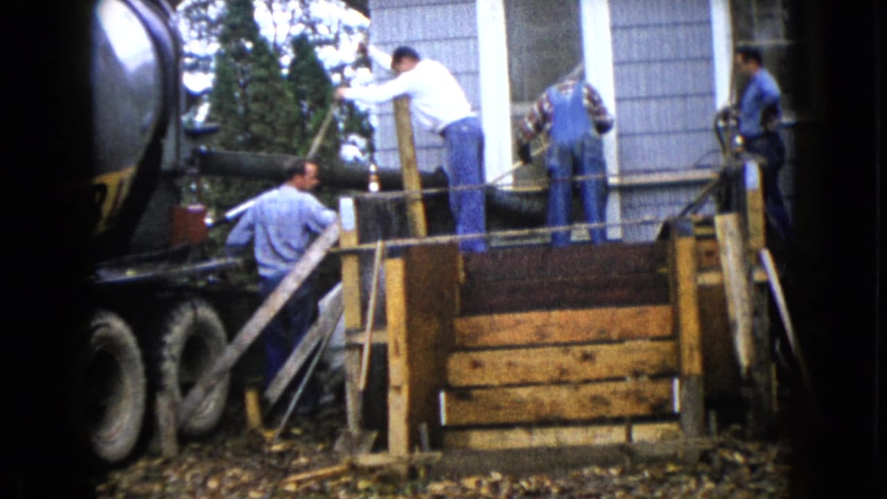 In Wauconda, Illinois, 1960, men in work clothes manage a concrete pour from a truck into wooden residential formwork.