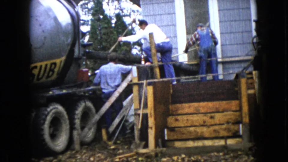 Workers in 1960s workwear stand around a concrete chute and formwork during a residential pour in Wauconda, Illinois.