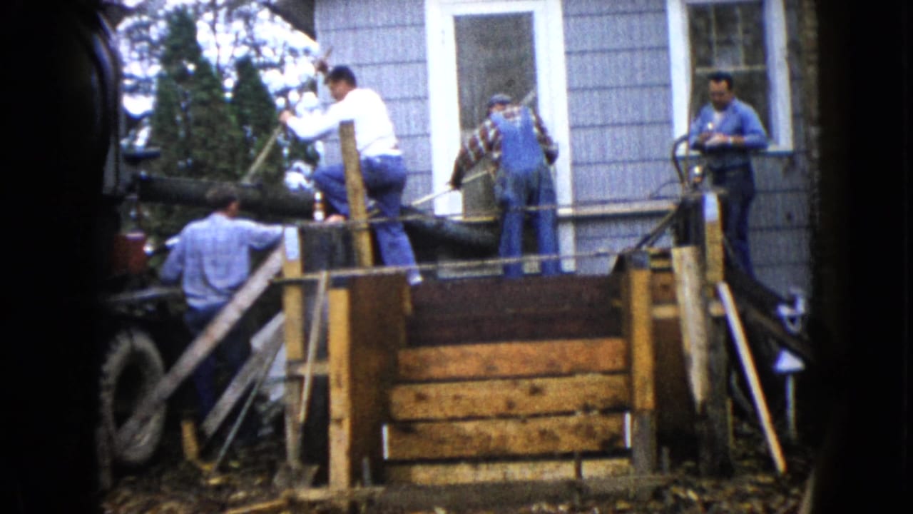 Men work around wooden porch framing outside a gray-sided house.