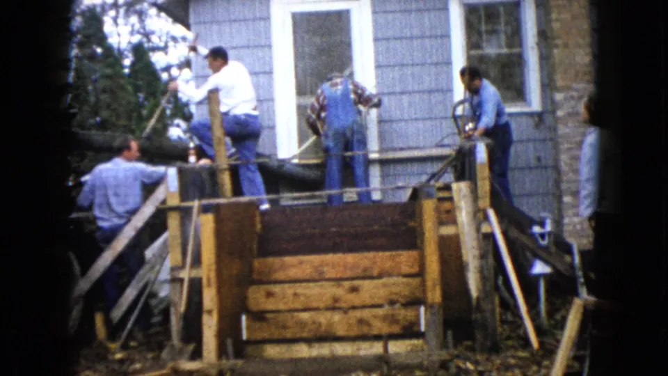 Men in shirts and overalls handle tools near wet cement on a porch frame outside a Wauconda house in 1960.