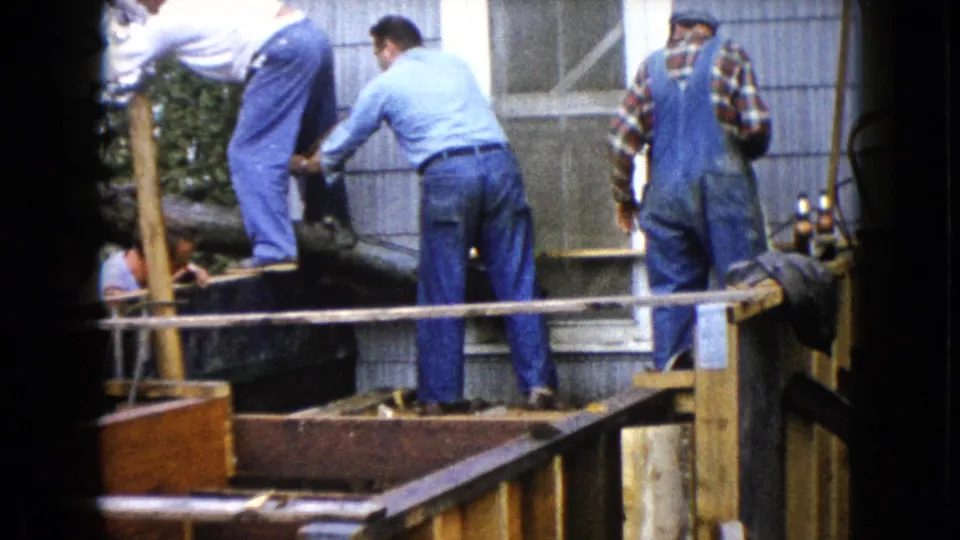Final frame shows men standing on and beside the porch form as cement work continues against the gray house exterior.