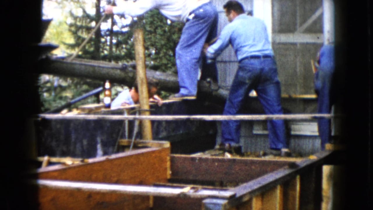 Men work around a porch area with shovels, wood framing, and fresh concrete near a house.