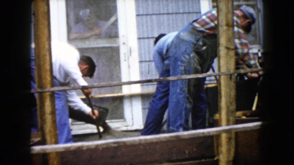 Men in casual work clothes shovel and spread wet concrete near a house doorway in 1960 Wauconda, Illinois footage.