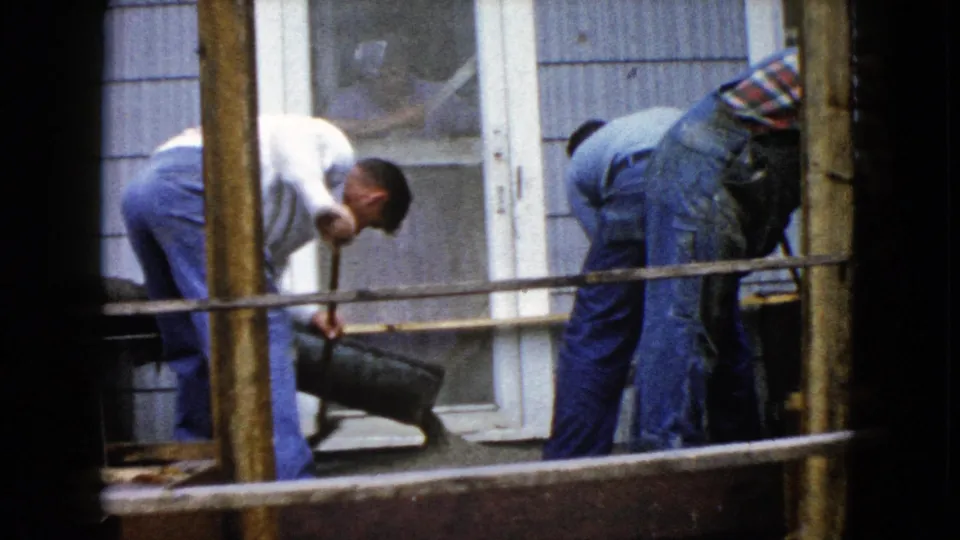 1960 Wauconda home construction frame with two men leaning over a porch pour beside a door and window.