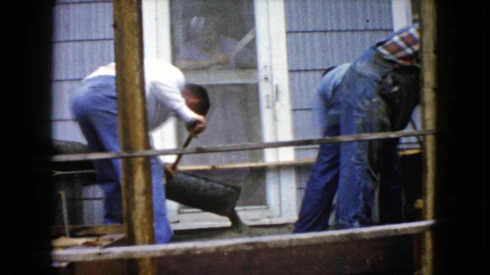 Men continue manual concrete work at a porch entrance in Wauconda, Illinois, seen through 8mm home-movie framing.