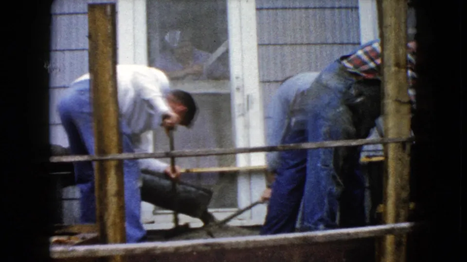 Two men continue residential cement work in Wauconda, Illinois, with the 8mm frame partly bordered by dark film edges.