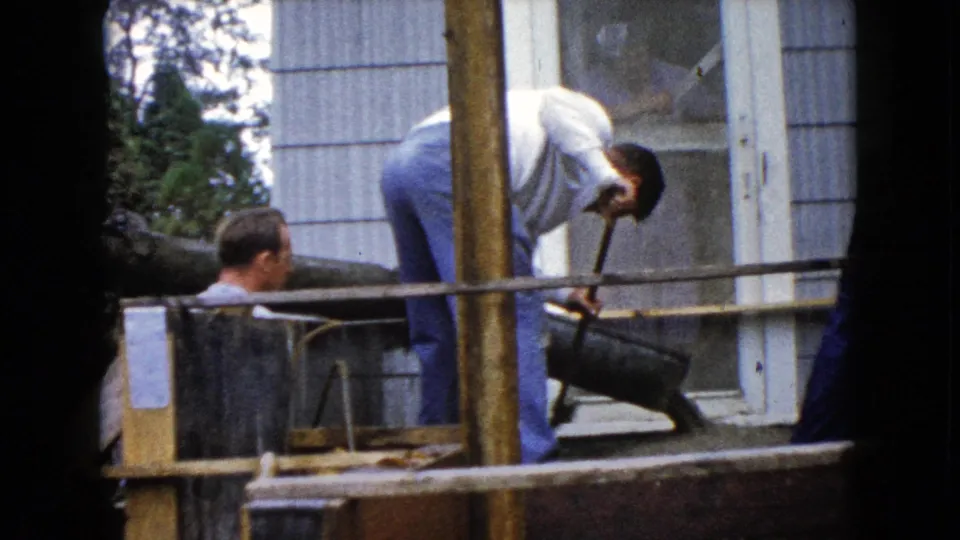A third man watches from the side as cement work continues outside a Wauconda house in this 1960 8mm home-movie frame.