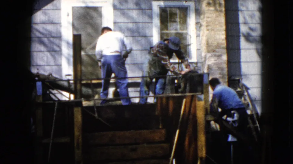 Three adult men continue porch repair work outside a Wauconda house, with one below the platform and two standing above.