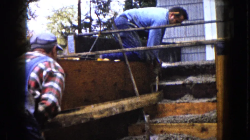 Two adult workers remain positioned around the wooden forms as the concrete step area is worked by hand in the 1960 Wauconda scene.
