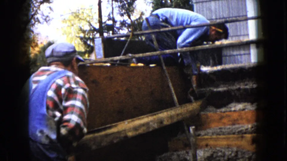 In the final frame, the man in blue remains bent over the form while the second man stands nearby, partially turned away from camera.