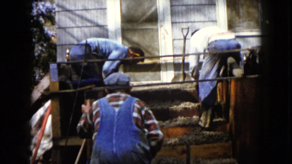 The 8mm frame shows adult men working over residential concrete forms in Wauconda, with a capped man standing below the steps.