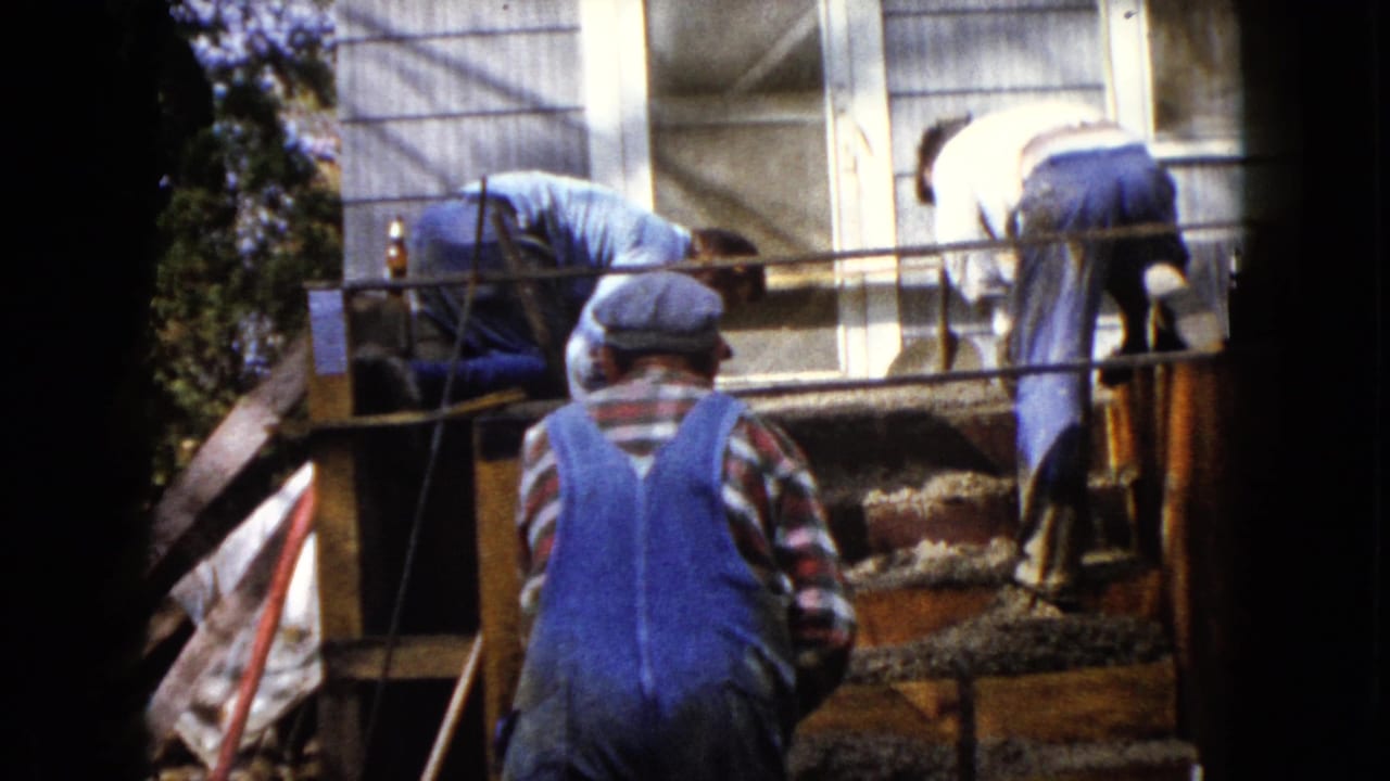 In 1960 Wauconda, Illinois footage, three workers bend over newly poured concrete steps outside a house.