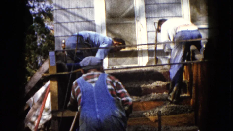 Workers in caps and overalls continue smoothing concrete steps outside a Wauconda house in 1960 home-movie footage.