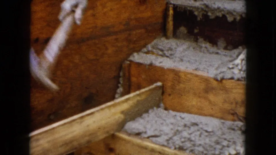 A raised gloved hand appears mid-swing over wooden framing and gray material in the 1960 Wauconda construction close-up.