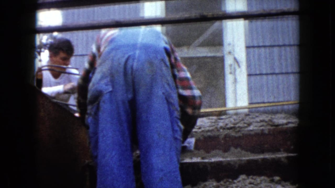 Worker in blue overalls leans over the stair forms with wet cement spread across the steps.