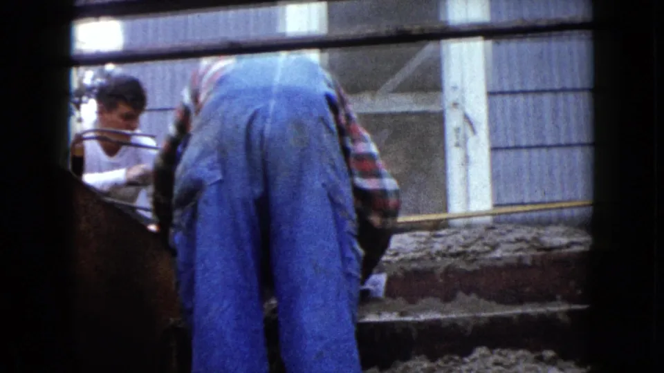 A close 8mm view of residential concrete stair work in Wauconda, with a worker in overalls centered and another man partly visible.