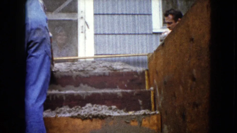 The final frame shows cement-covered stair forms outside the Wauconda house, with workers partly cropped by the handheld camera.