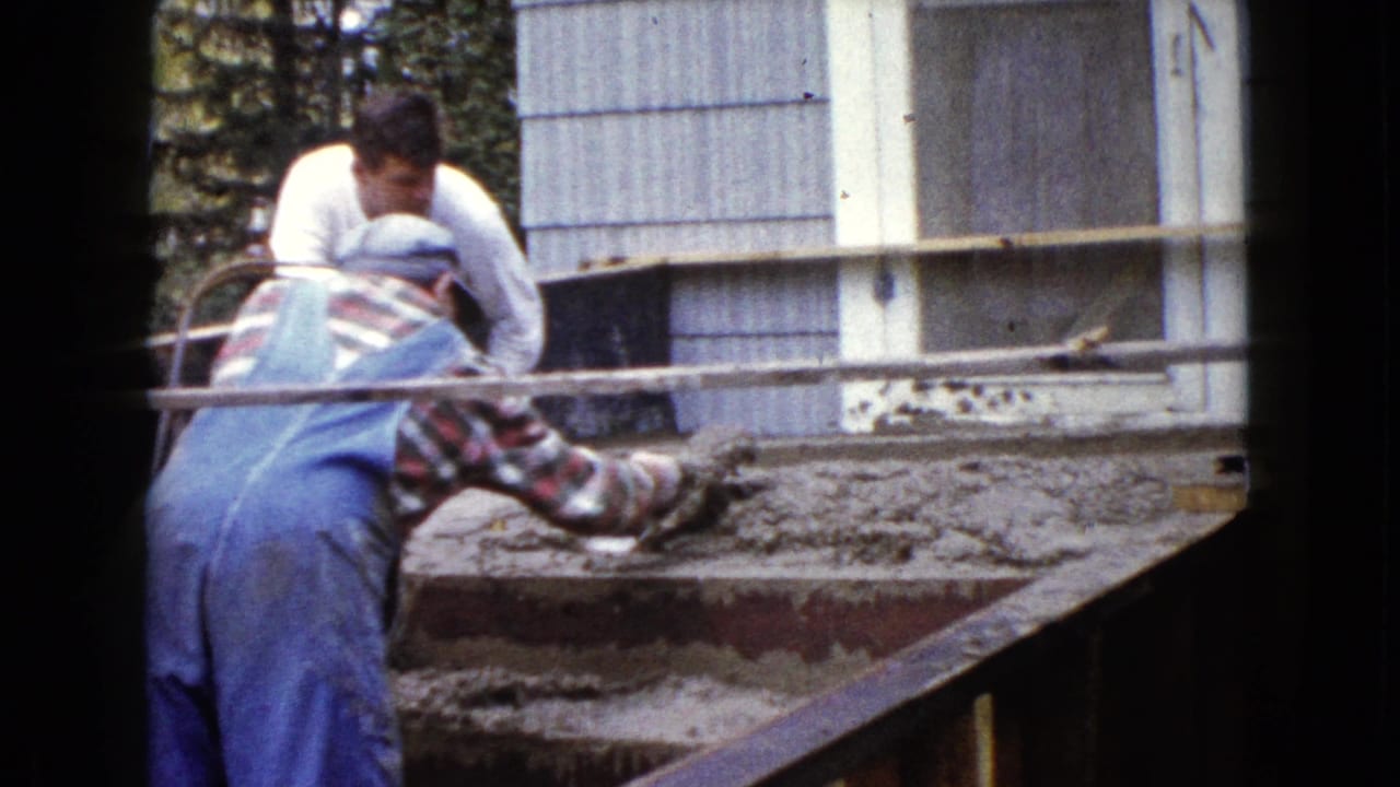 A man in blue overalls uses a trowel on wet concrete stairs as another man assists outside a Wauconda residence.