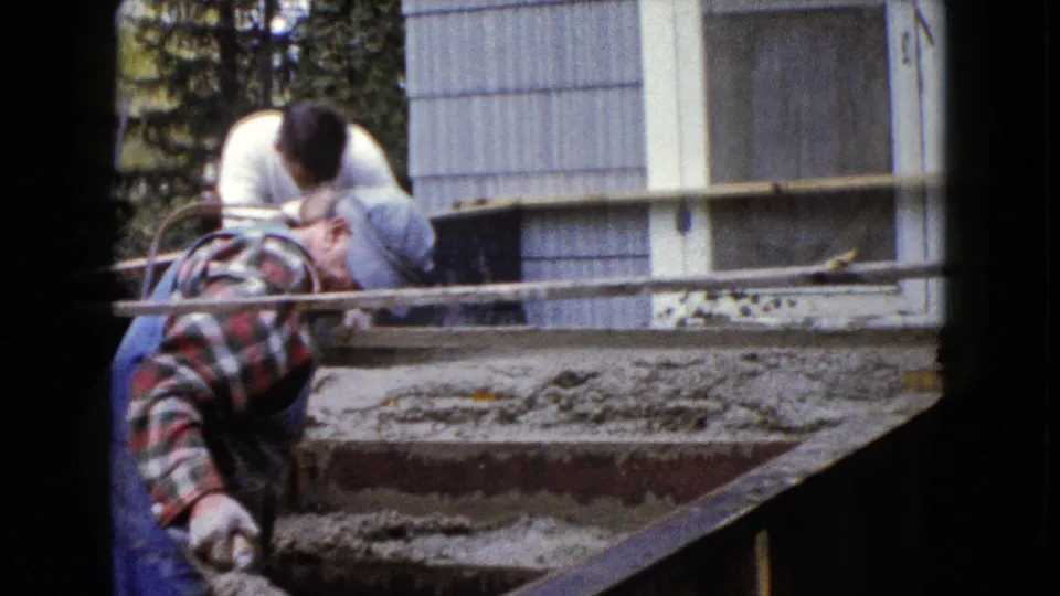 Late frame of the Wauconda stair repair shows a man finishing wet concrete with a trowel below a metal railing.