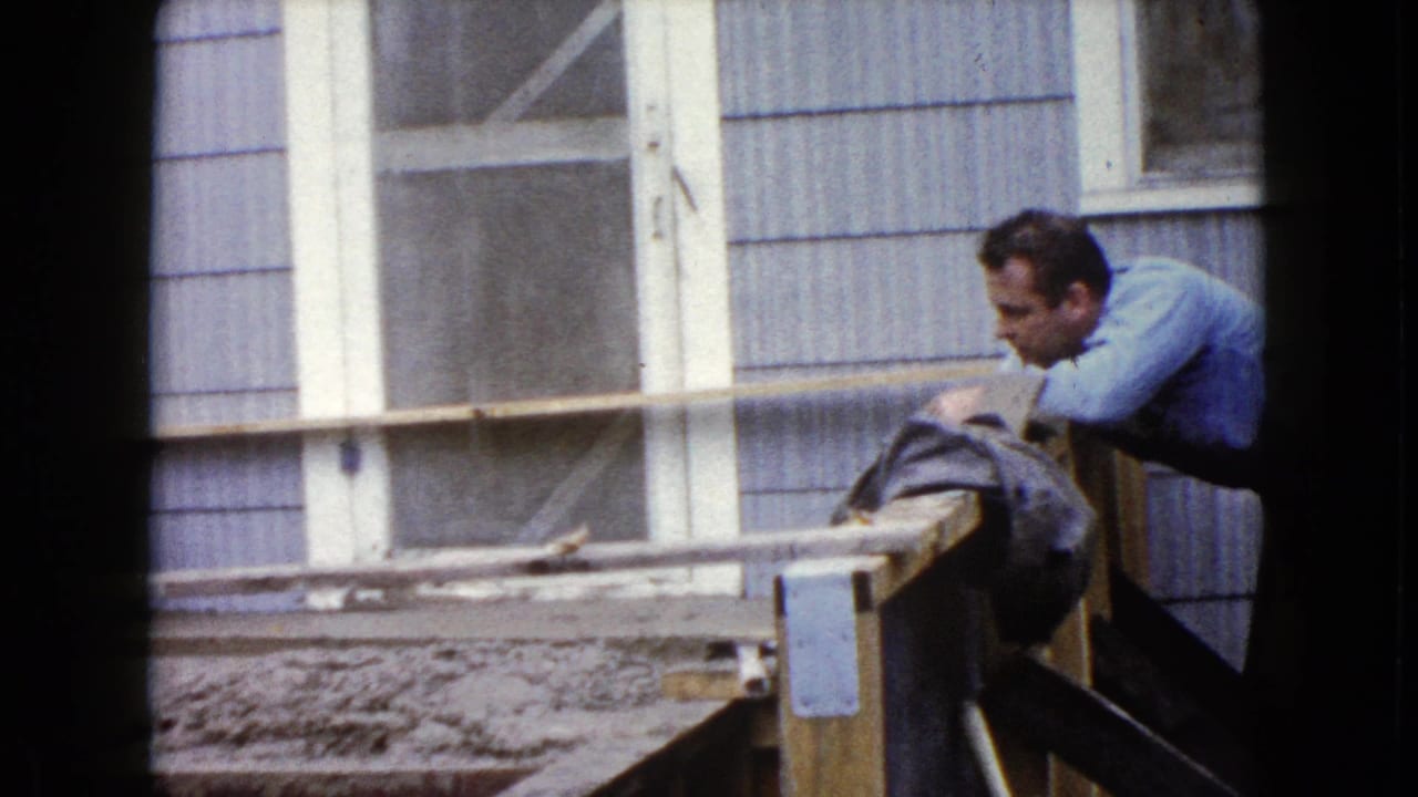 A man in a blue shirt leans over the railing near the cement steps outside the Wauconda residence, with windows behind him.