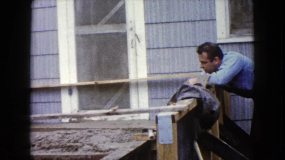 A man in a blue shirt leans over the railing near the cement steps outside the Wauconda residence, with windows behind him.