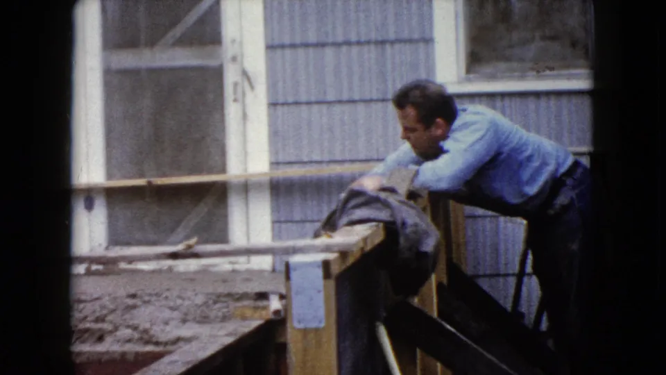 A man in work clothes bends over a wooden step form during a 1960 residential concrete project in Wauconda, Illinois.