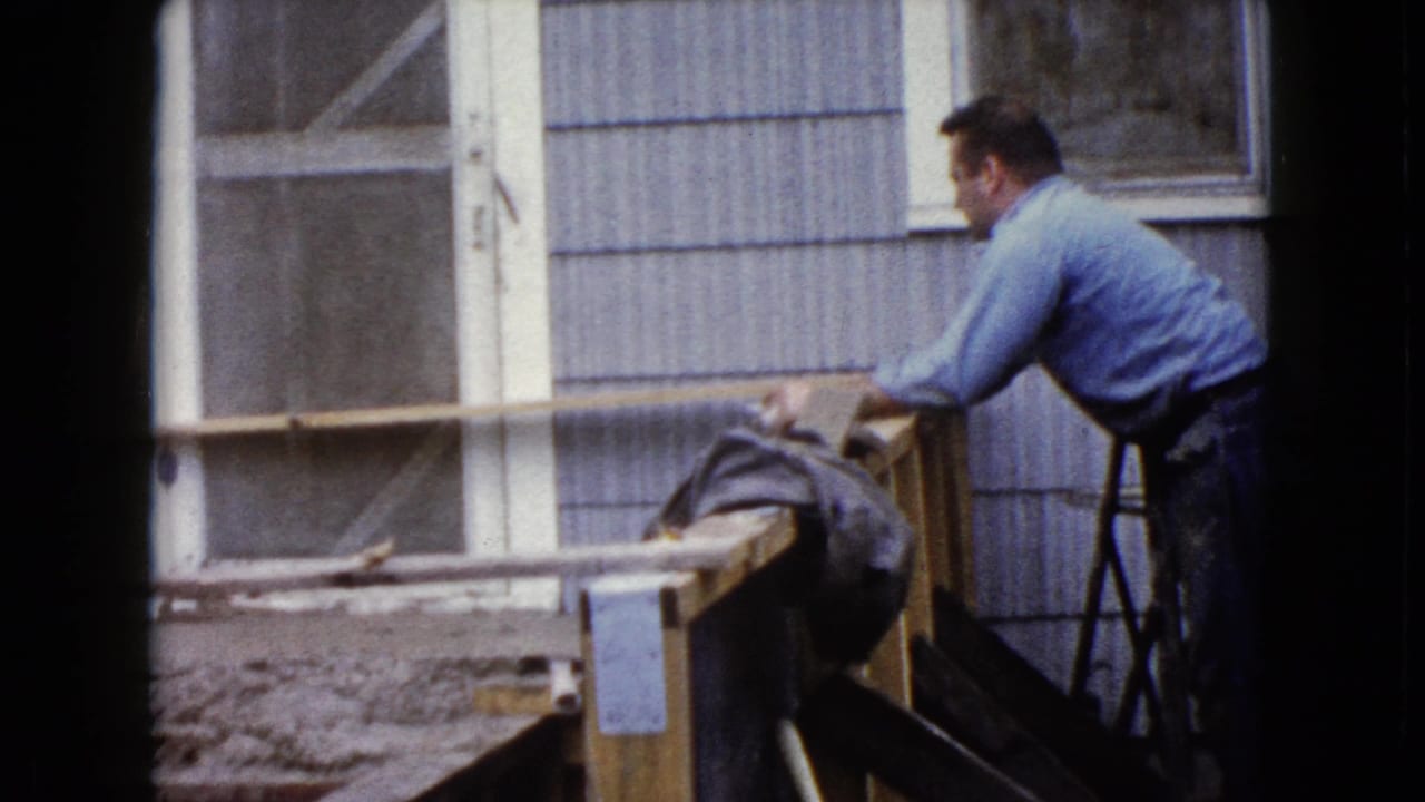 The 8mm frame shows a side view of a man shaping concrete steps against a residential exterior in Wauconda, Illinois.