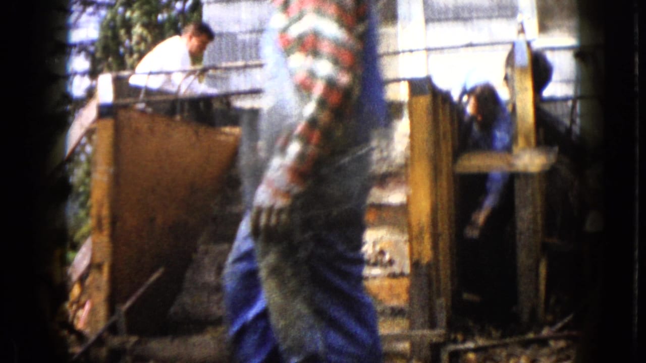 A man in a white shirt leans over wooden forms while another worker is partly visible inside the structure.