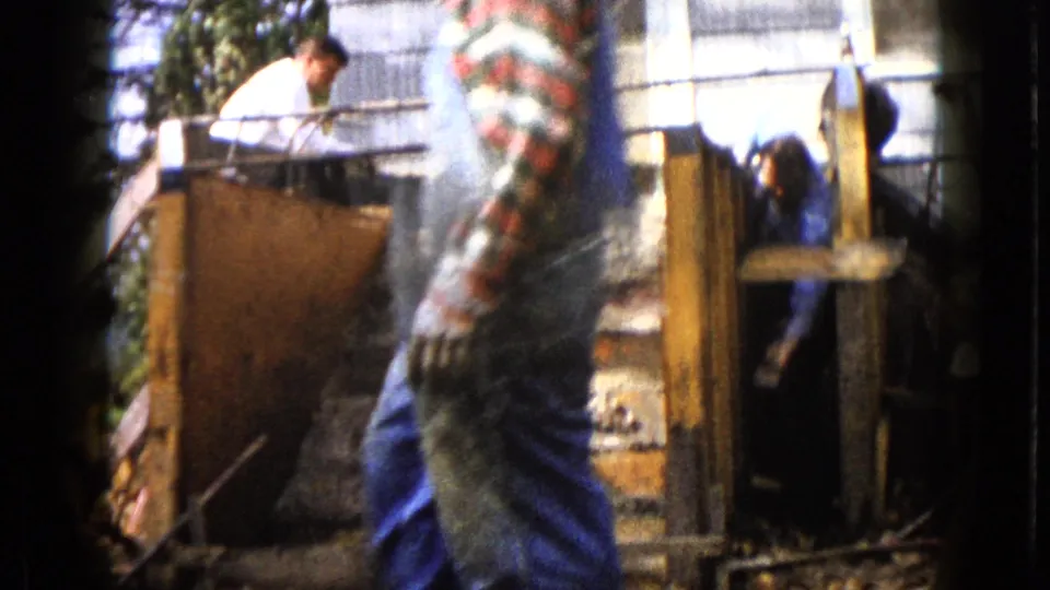 1960 Wauconda home-movie frame showing a man leaning over concrete step formwork with another worker partly hidden inside.