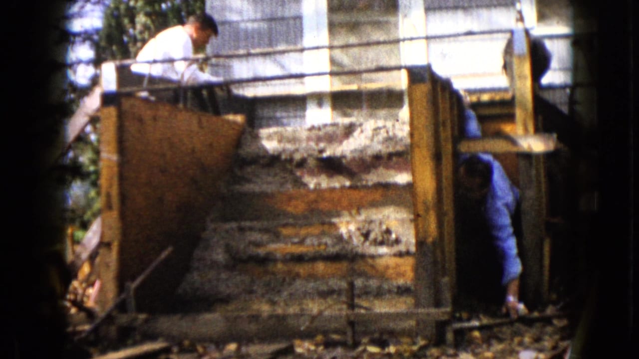 1960 Wauconda construction frame showing men around wooden forms and unfinished concrete steps beside a house.