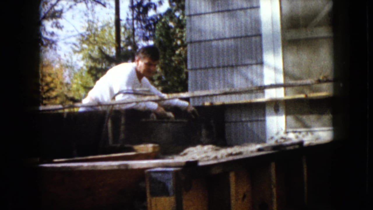 A man in a white shirt turns slightly toward the camera during backyard work in the supplied 1960 Wauconda setting.