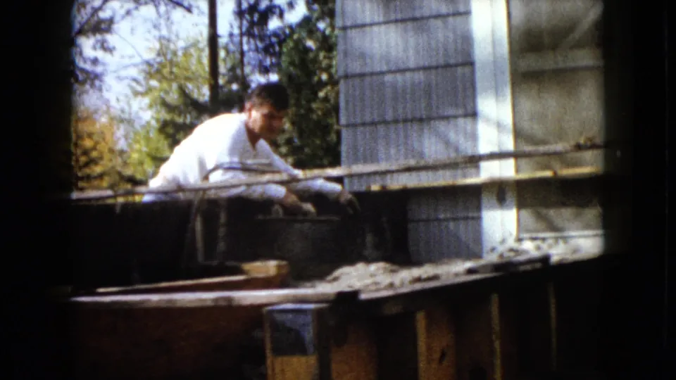 A man in a white shirt turns slightly toward the camera during backyard work in the supplied 1960 Wauconda setting.