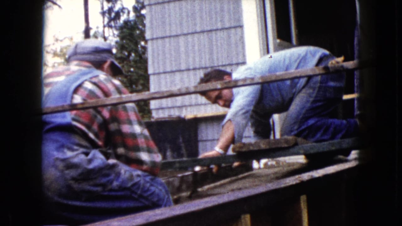 1960 Wauconda 8mm frame showing men working on a porch frame near the house exterior and open doorway.