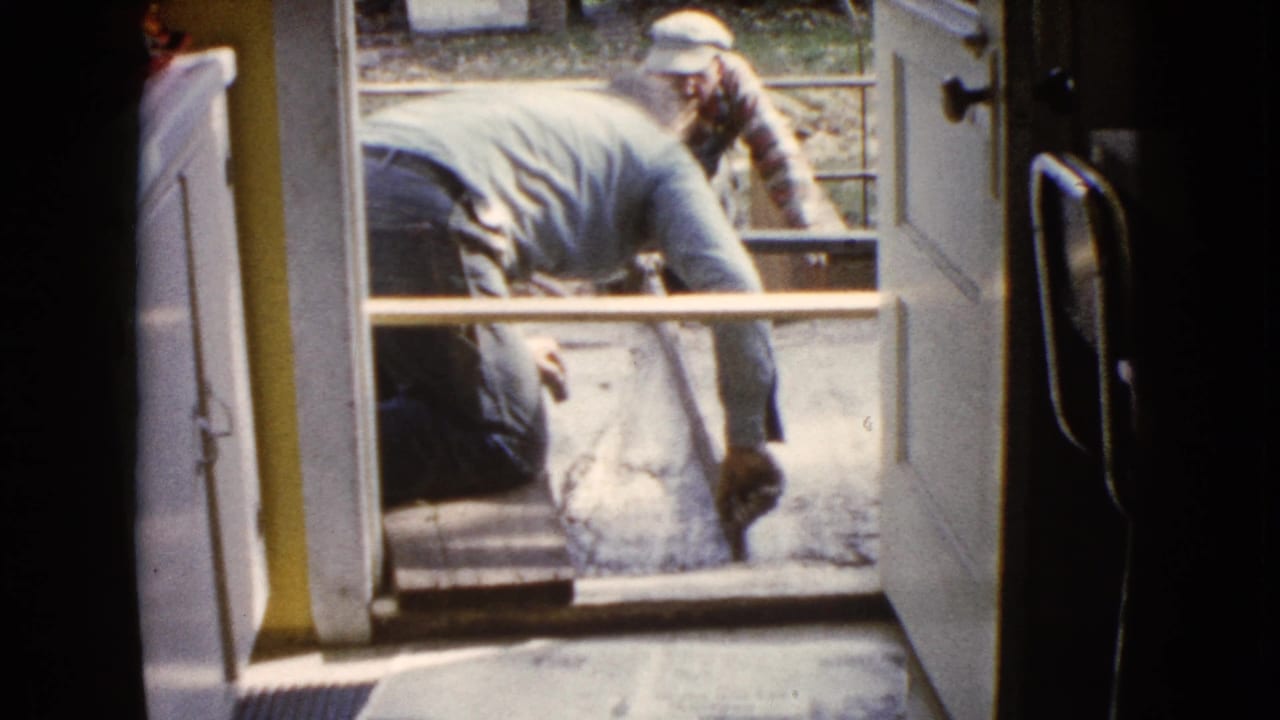 A man bends over the porch threshold while another man works beyond the open door.