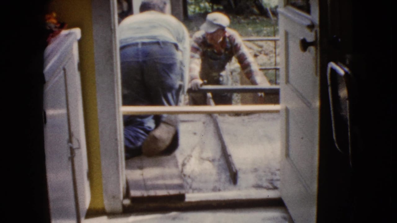 1960 Wauconda 8mm frame with a kneeling worker inside the doorway and another man handling porch concrete outside.
