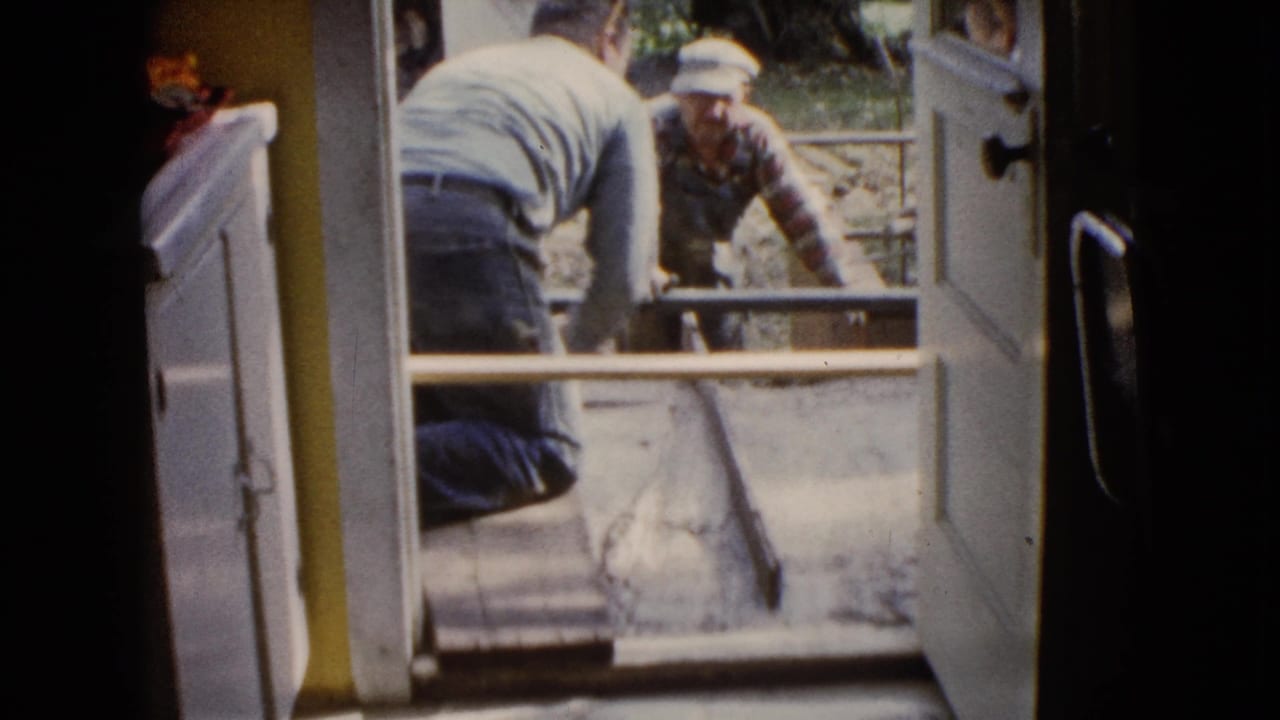 Two men work on wet cement outside an open doorway.