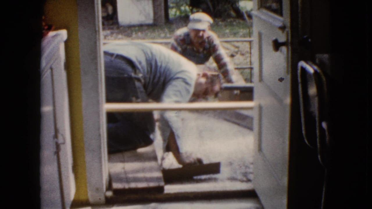 Viewed from inside, a man smooths wet cement near the threshold while a second man assists outside in Wauconda, Illinois.