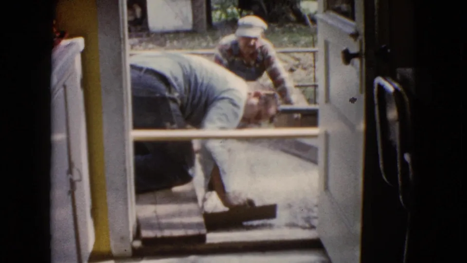 Viewed from inside, a man smooths wet cement near the threshold while a second man assists outside in Wauconda, Illinois.