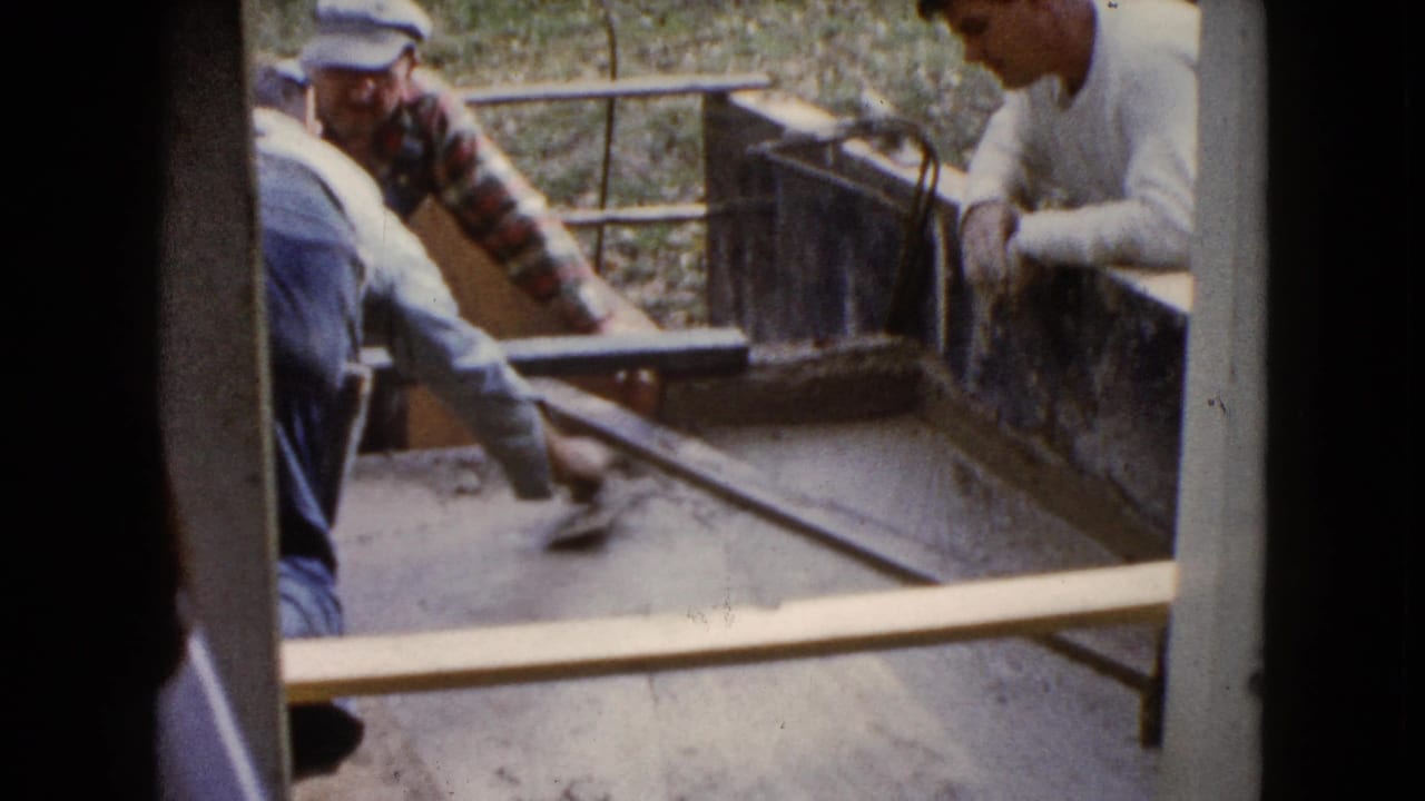 Older men in work clothes continue smoothing cement in a rectangular form in Wauconda, Illinois, in 1960 footage.