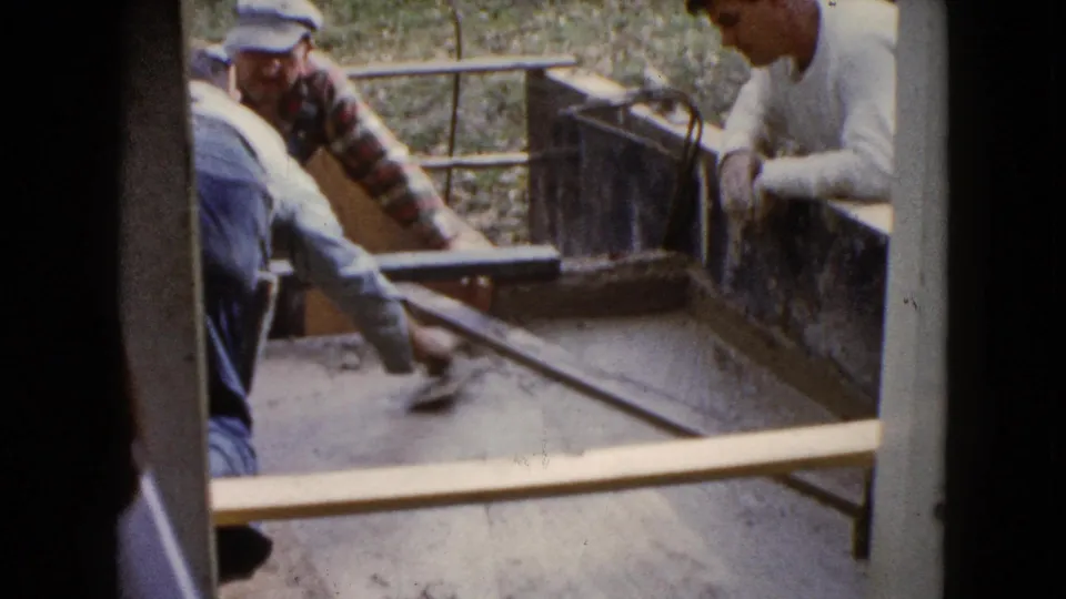 Older men in work clothes continue smoothing cement in a rectangular form in Wauconda, Illinois, in 1960 footage.