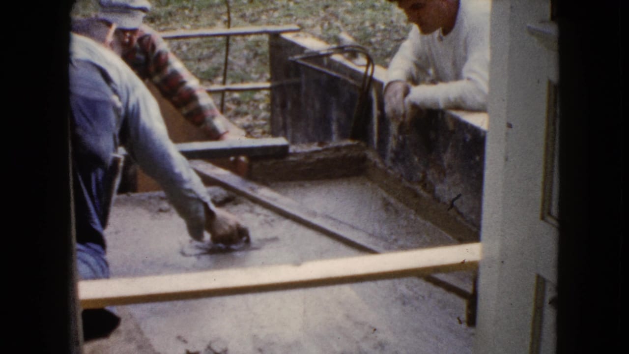Two men work over a concrete form viewed through a doorway.
