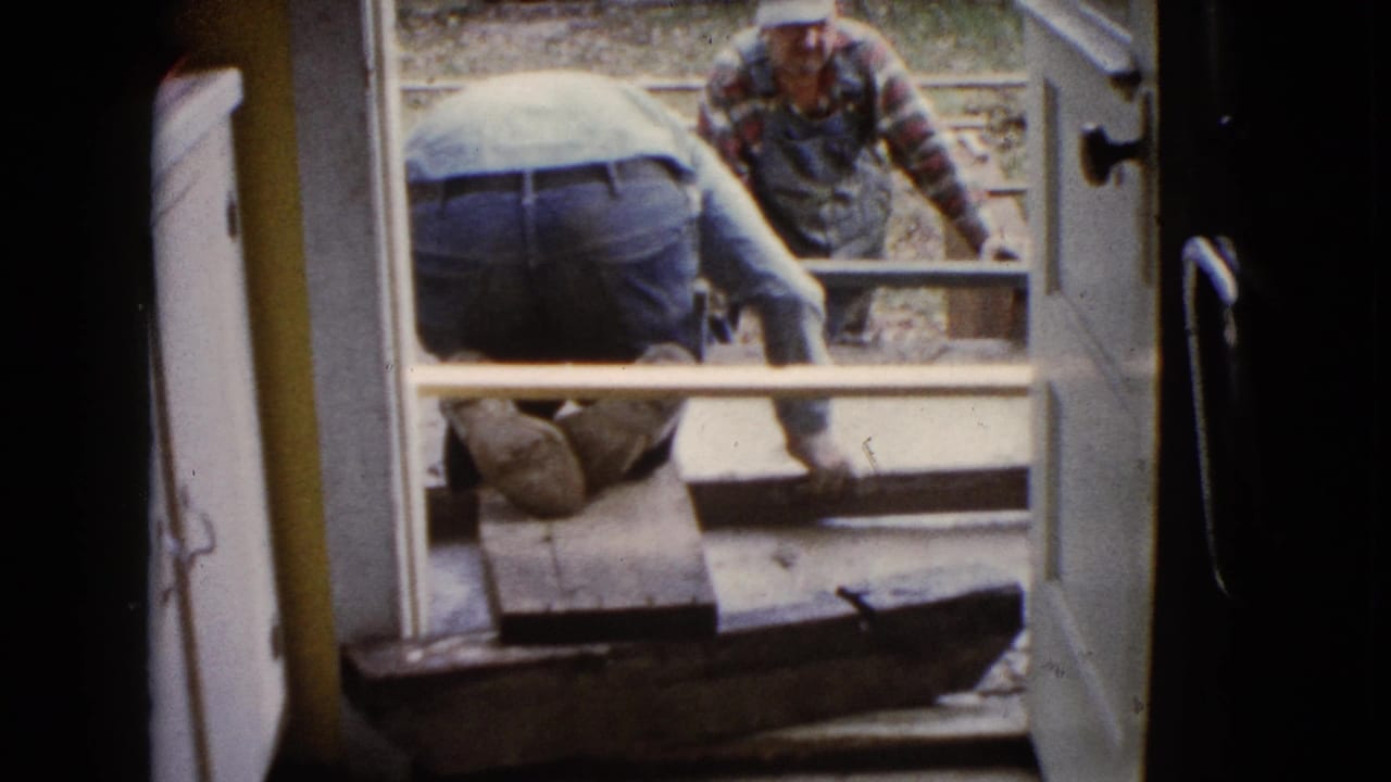 1960 Wauconda home-movie frame showing men repairing a porch or patio surface through a doorway.