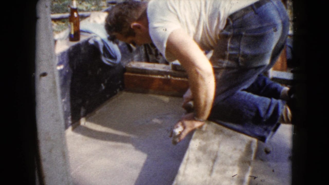 The 8mm frame shows a kneeling man working a trowel over fresh cement on a porch or patio in Wauconda.